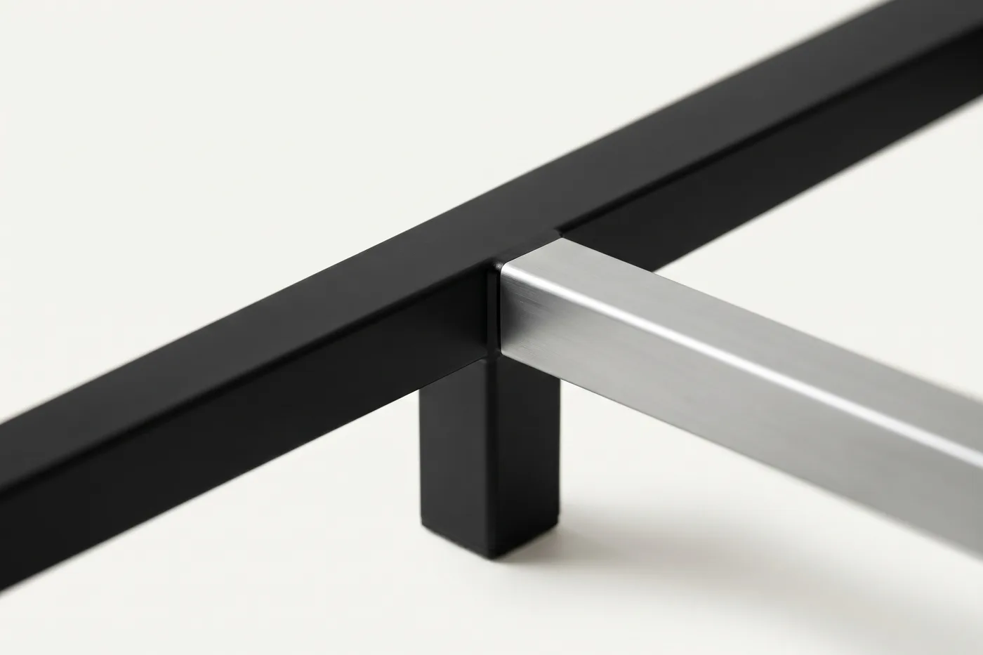 Smooth powder-coated black steel desk frame meeting a satin aluminum beam